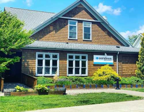 A charming brown wooden building with a sign reading "Cerulean" and landscaped greenery in front.