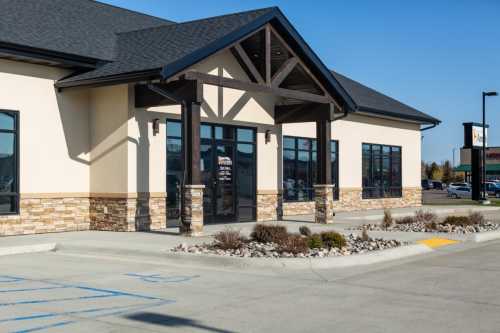 A modern commercial building with a stone facade and large windows, set against a clear blue sky.