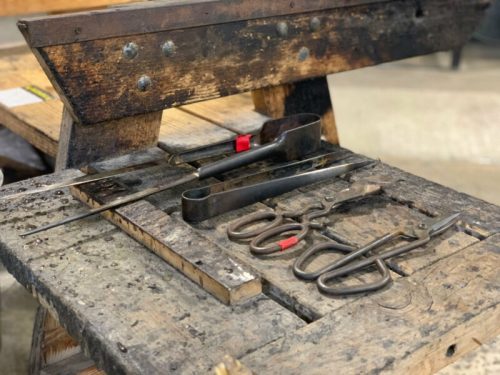 A wooden workbench with various metal tools, including scissors and tongs, resting on its surface.