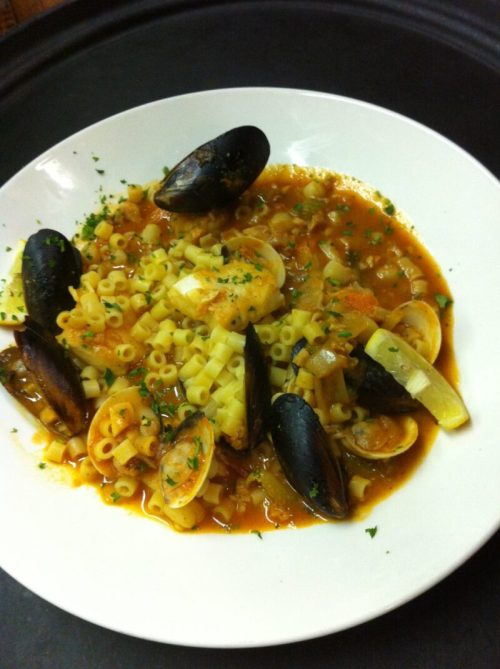 A bowl of pasta with clams and mussels in a rich tomato sauce, garnished with herbs.