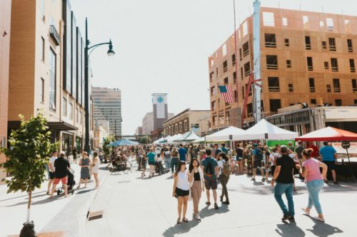 A bustling street market with crowds, tents, and buildings under construction on a sunny day.