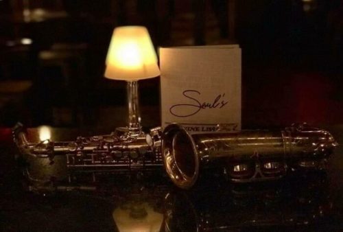 A saxophone and a menu titled "Soul's" sit on a dark table beside a glowing lamp.