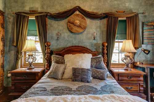 Cozy bedroom with a wooden bed, decorative pillows, elegant lamps, and rich blue-green walls.