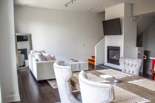 Modern living room with a sofa, dining table, and a fireplace, featuring neutral colors and a wall-mounted TV.