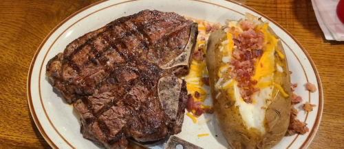 A plate featuring a grilled steak alongside a loaded baked potato topped with cheese, bacon, and chives.