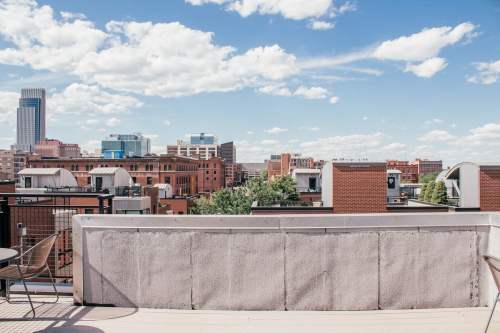 A rooftop view of a city skyline with buildings and a blue sky dotted with clouds.