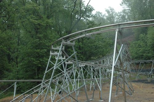 A partially constructed roller coaster track surrounded by lush green trees on a misty day.