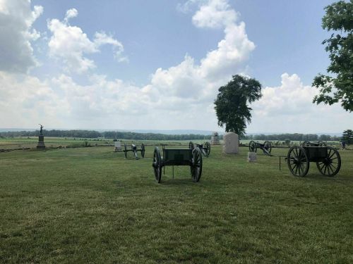 A grassy field with several historical cannons and a monument under a partly cloudy sky.