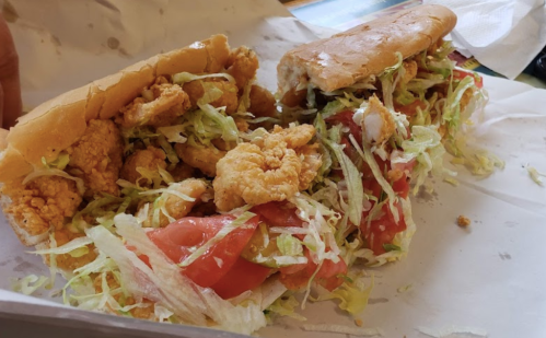 A sandwich filled with crispy chicken, lettuce, and tomato, served in a soft bun on a white paper background.