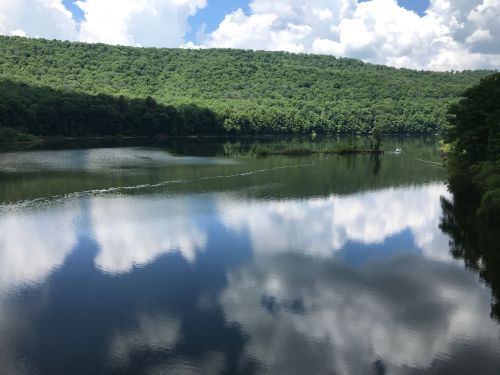 A serene lake surrounded by lush green hills, reflecting fluffy clouds in the calm water.