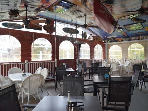 A cozy restaurant interior with tables and chairs, featuring a colorful ceiling and large windows.