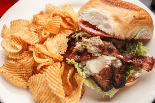 A sandwich with layers of bacon, lettuce, and tomato, served with a side of wavy potato chips on a white plate.