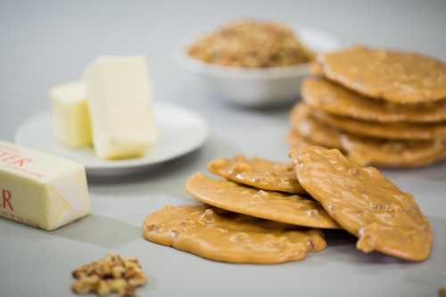 A plate of nutty candy, butter, and a bowl of oats, with additional candy pieces in the foreground.