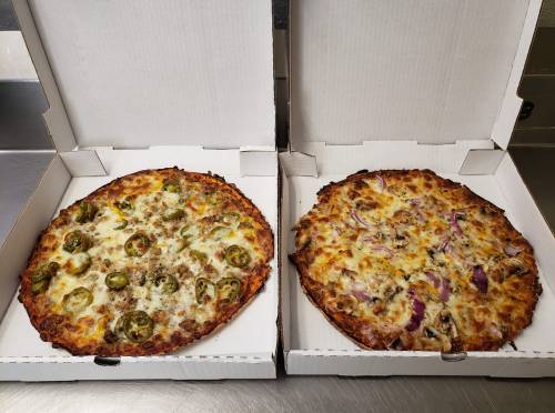 Two pizza boxes open, one with jalapeño and sausage pizza, the other with onion and chicken pizza.