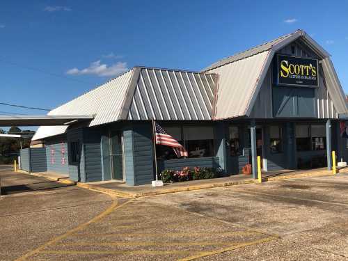 Exterior of Scott's restaurant with a metal roof, American flag, and flower beds, set against a clear blue sky.