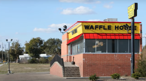 A Waffle House restaurant with a bright yellow sign, red roof, and large windows, set against a clear blue sky.
