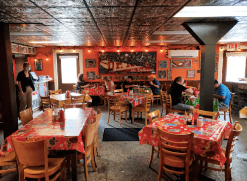 A cozy restaurant interior with colorful tablecloths, wooden chairs, and patrons enjoying their meals. Warm lighting enhances the atmosphere.