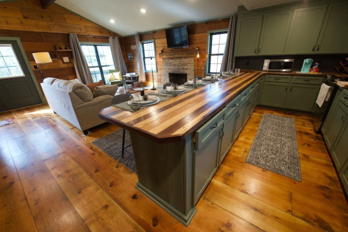 A cozy kitchen with a wooden island, green cabinets, and a living area featuring a sofa and fireplace.