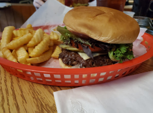 A juicy hamburger with lettuce, tomato, and cheese, served with crinkle-cut fries in a red basket on a wooden table.