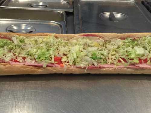 A long sub sandwich filled with layers of meats, lettuce, tomatoes, and seasonings on a countertop.