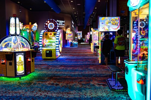A vibrant arcade with colorful games and glowing lights, featuring various machines and players enjoying the space.