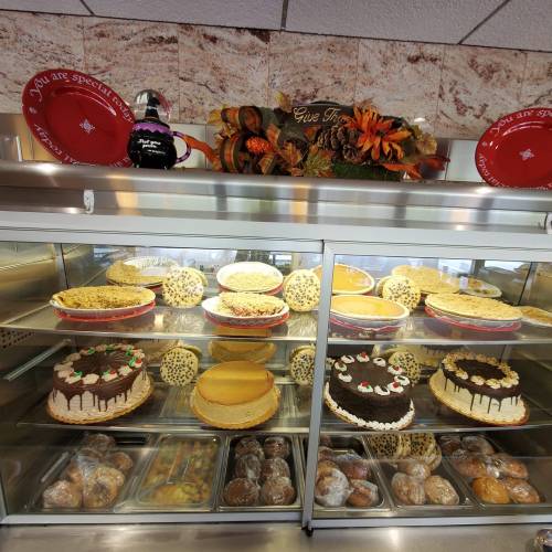 A display case filled with various cakes and desserts, topped with a decorative autumn arrangement.