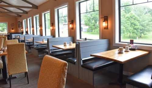 Cozy restaurant interior with wooden booths and tables, large windows, and soft lighting.