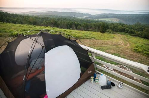 A tent set up on a deck overlooking a misty valley and rolling hills at dawn.