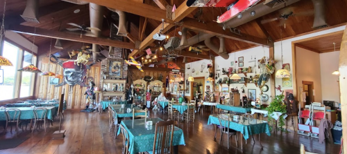 A spacious restaurant interior with wooden beams, eclectic decor, and tables set with green tablecloths.
