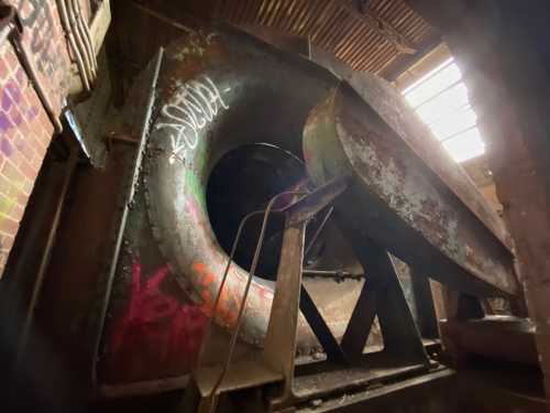 An industrial turbine with rust and graffiti, set in a dimly lit, brick-walled space.