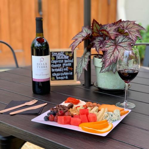 A wine bottle, glass, and a platter of assorted cheeses, fruits, and charcuterie on a table with a plant in the background.
