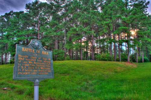 Historical marker for the Battle of Iuka, surrounded by trees, detailing the 1862 Civil War clash in Mississippi.