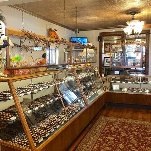 A cozy chocolate shop display featuring various chocolates in glass cases, with warm wooden decor and a chandelier.