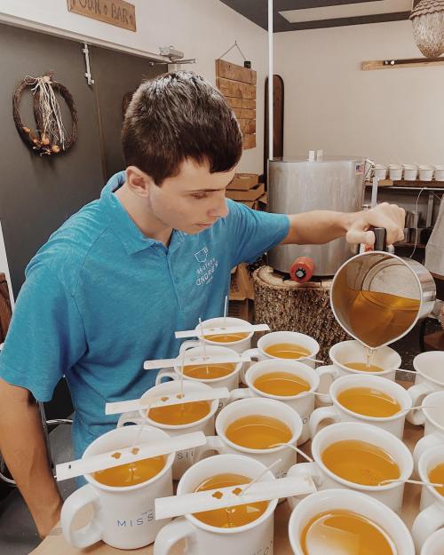 A person in a blue shirt pours tea into multiple white cups arranged on a table.