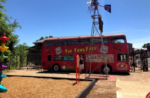 A colorful double-decker bus, "The Funky Yard," next to a playground with a windmill and climbing structures.