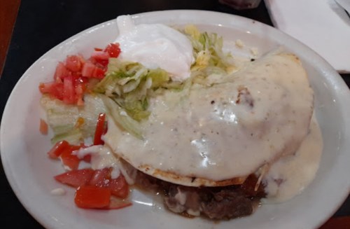 A plate of food featuring a taco topped with creamy sauce, lettuce, diced tomatoes, and a dollop of sour cream.