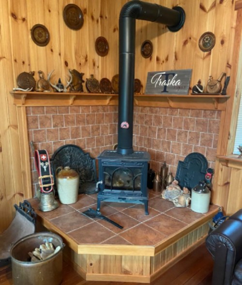 Cozy wooden room featuring a black stove, decorative wall plates, and a rustic hearth with various ornaments.