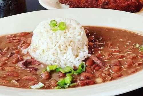 A plate of rice topped with green onions, served with a rich bean stew and garnished with chopped herbs.