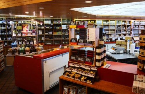 A well-stocked store interior featuring shelves of jars, bottles, and packaged goods, with a checkout area visible.