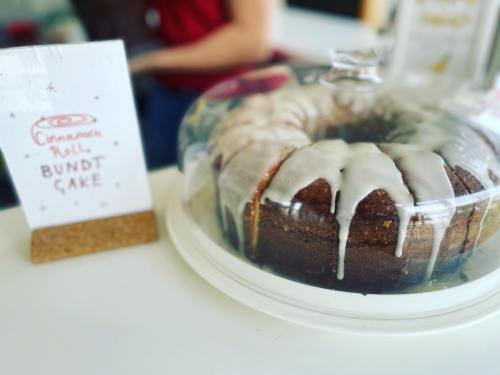 A cinnamon roll bundt cake under a glass dome, with a sign displaying its name beside it.