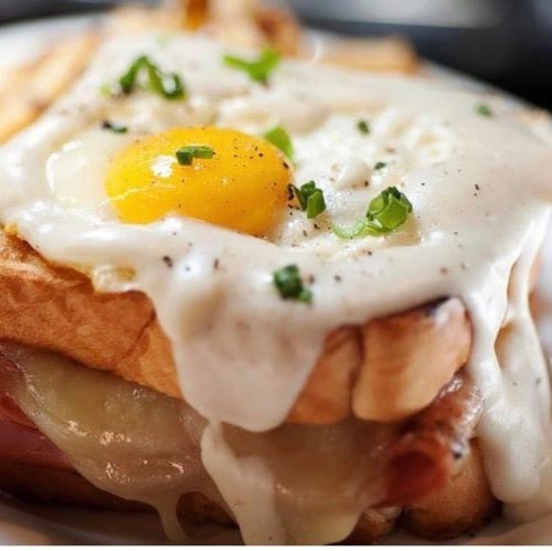 A close-up of a toasted sandwich topped with melted cheese, a sunny-side-up egg, and green onions.