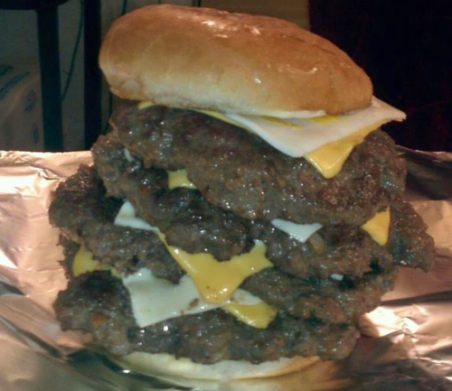 A towering burger with multiple beef patties, melted cheese, and a soft bun, resting on foil.