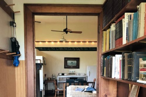 A cozy room with a ceiling fan, bookshelves, and a dining area visible through an open doorway.