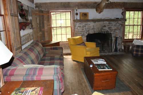 Cozy rustic living room with a plaid sofa, yellow armchair, wooden coffee table, and stone fireplace.