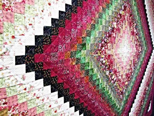 A colorful quilt featuring a geometric pattern of squares in shades of pink, green, and white, creating a vibrant design.