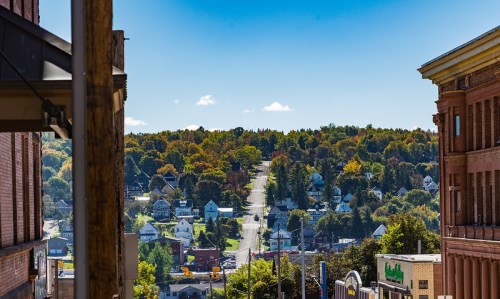 A scenic view of a tree-lined street with houses, framed by buildings under a clear blue sky.