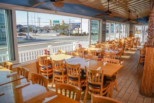 Bright restaurant interior with wooden tables and chairs, large windows overlooking a street and outdoor scenery.