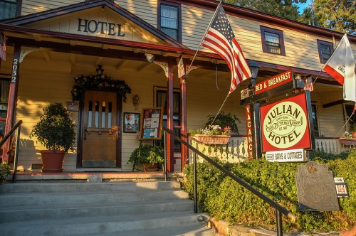A charming hotel entrance with flags, a sign for a bed and breakfast, and a welcoming porch adorned with plants.