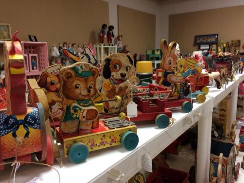 Colorful vintage toy animals on wheels displayed on a shelf, including a bear, dog, rabbit, and girl.
