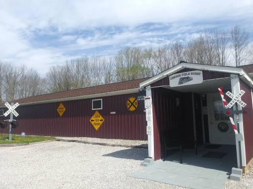 A red barn-like building with railroad signs and a gravel path, surrounded by trees under a blue sky.